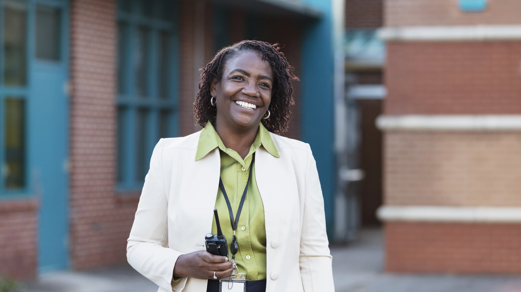 An administrator holding a walkie talkie smiles outside a building